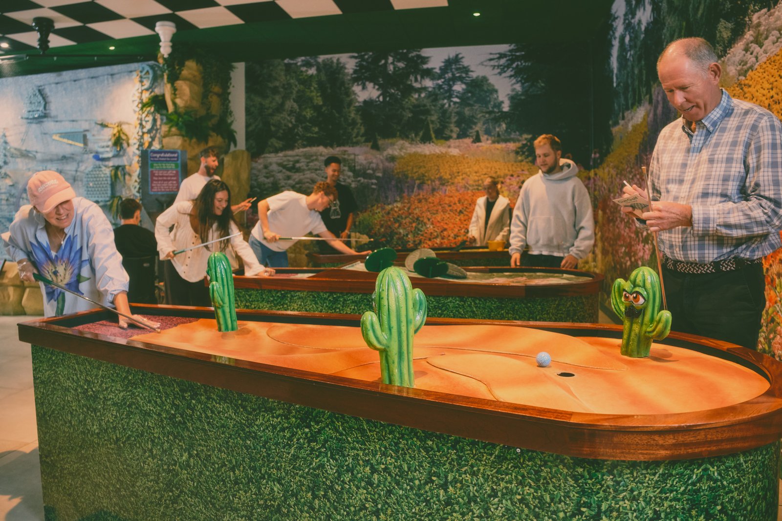 Guy Topping on the floor at the Flower Bowl's Cue Golf cactus hole, scorecard in hand